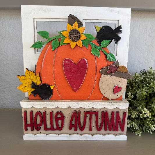 Decorative autumn-themed sign with a pumpkin, leaves, and text on a neutral background.