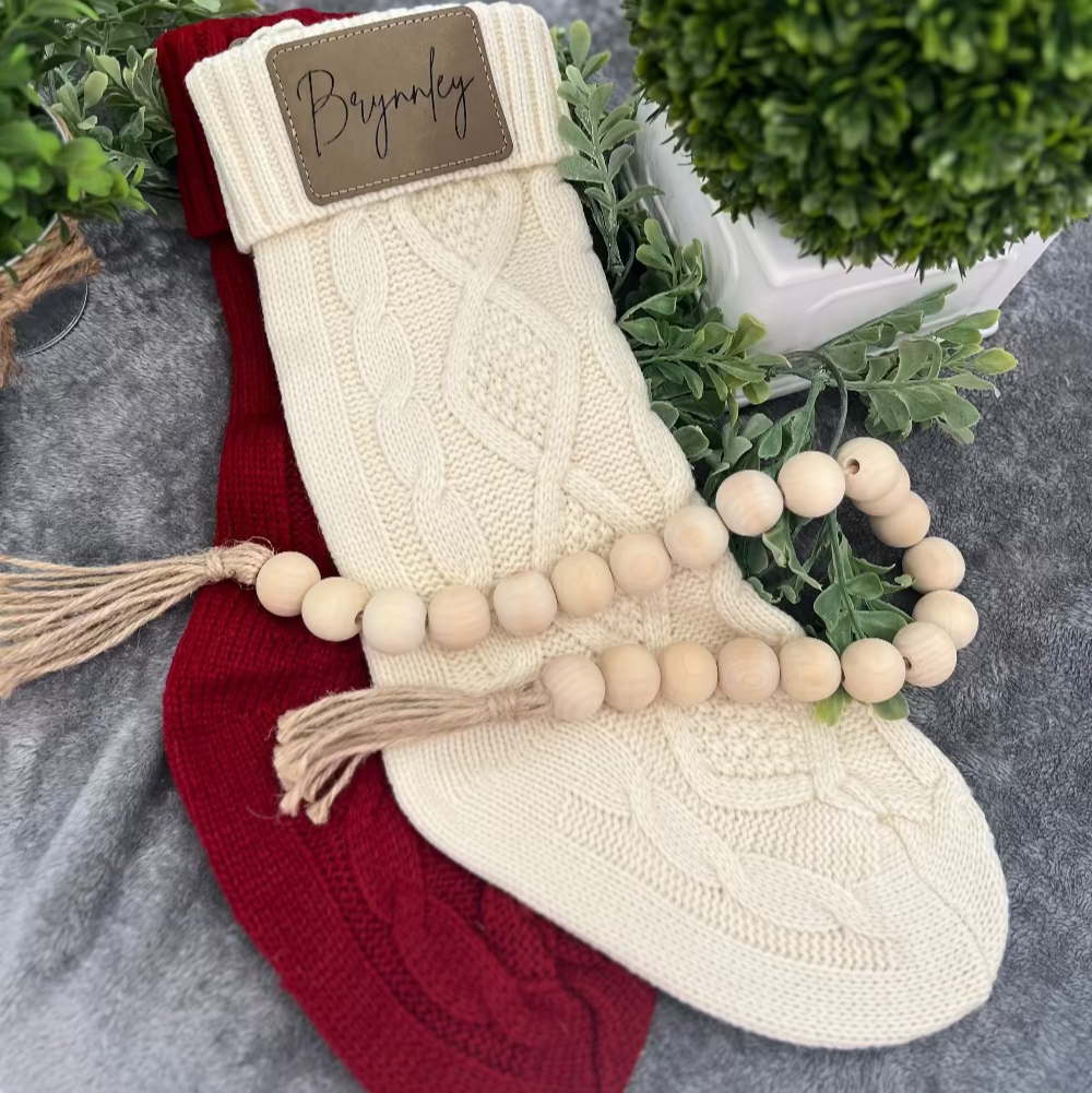 Two knitted stockings, one red and one cream, with a wooden bead garland on a gray surface.