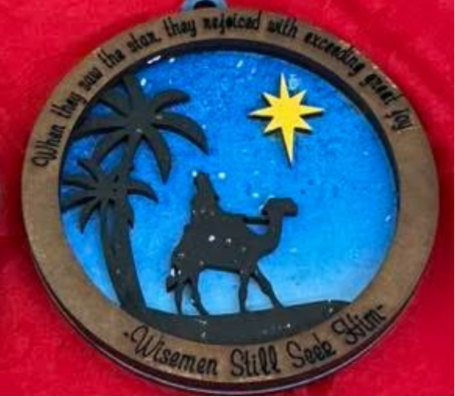 Decorative ornament with nativity scene, palm trees, and star on a blue background.
