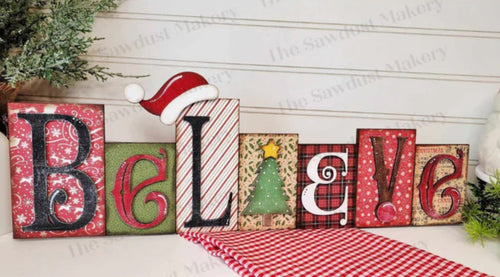 Christmas-themed decorative letters spelling 'BELIEVE' on a wooden surface with festive decorations.