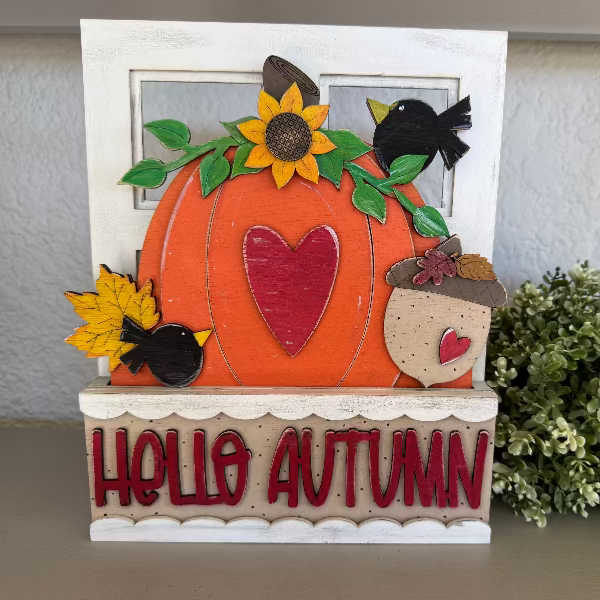 Decorative autumn-themed sign with a pumpkin, leaves, and text on a neutral background.
